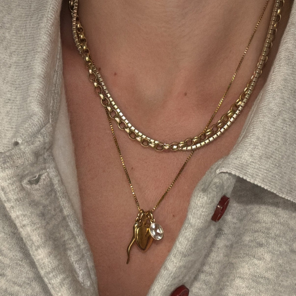 Close-up of a person wearing a gold necklace with a heart locket pendant and a tennis necklace layered