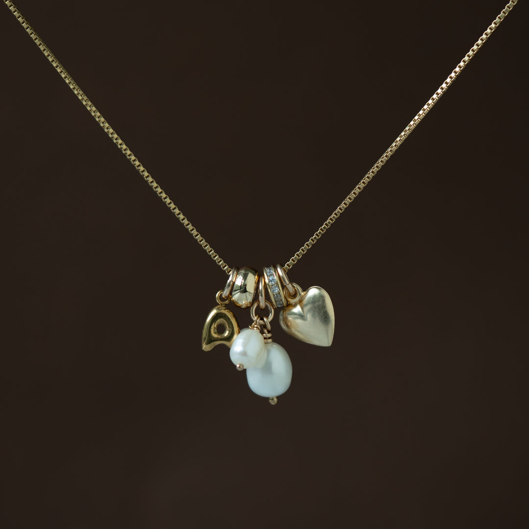 Necklace with heart, fish, and pearl charm on a dark background