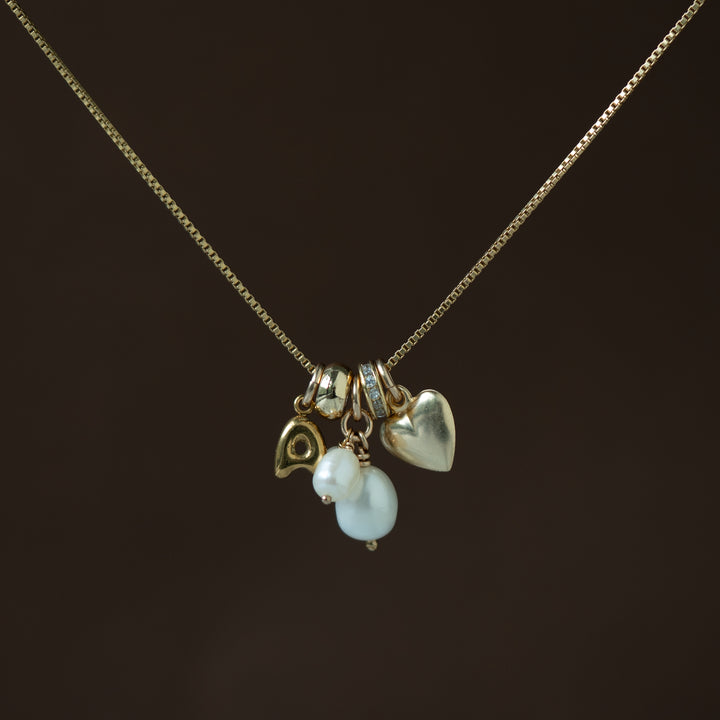Necklace with heart, fish, and pearl charm on a dark background