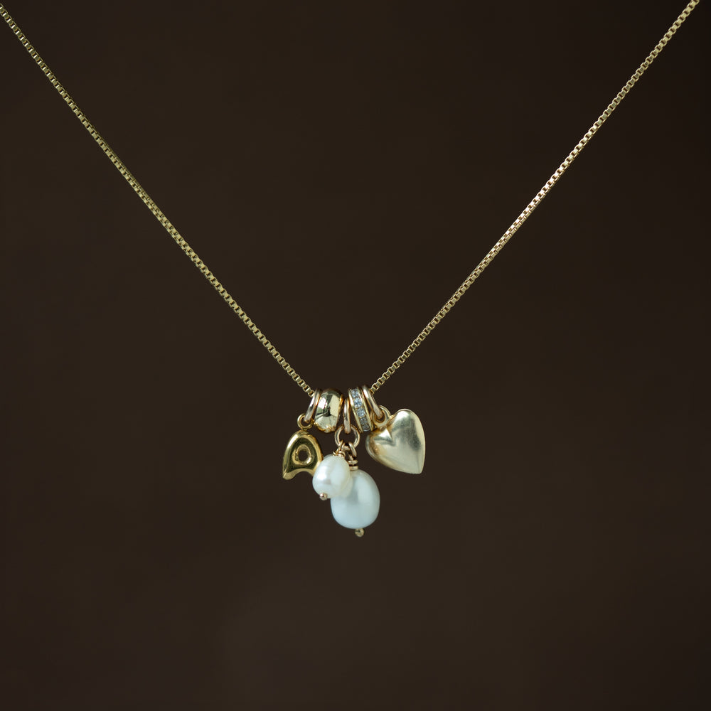 gold necklace with gold and pearl charms on a dark brown background