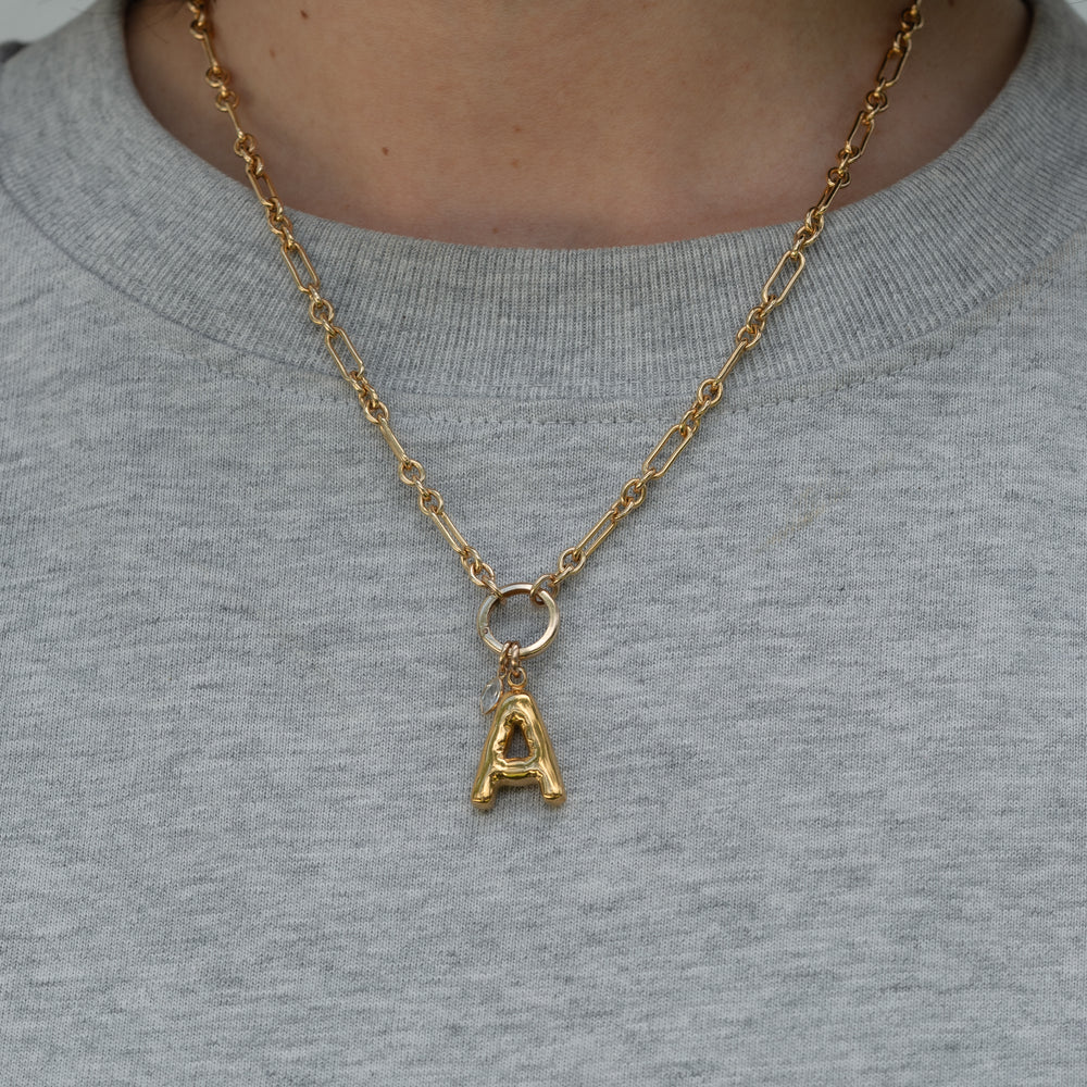 Gold necklace with a letter 'A' pendant & marquise pendant on a gray shirt