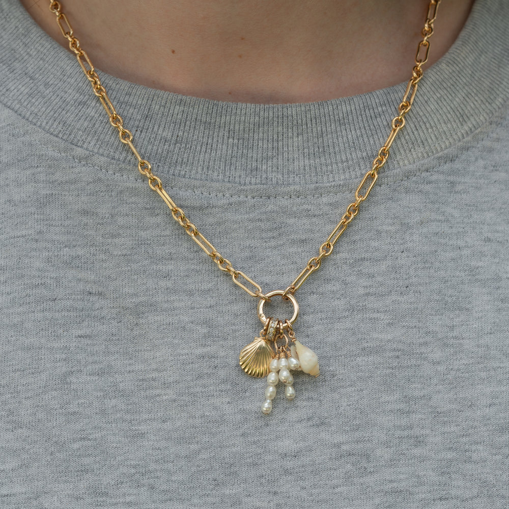 Gold necklace with shell and pearl charms on a person