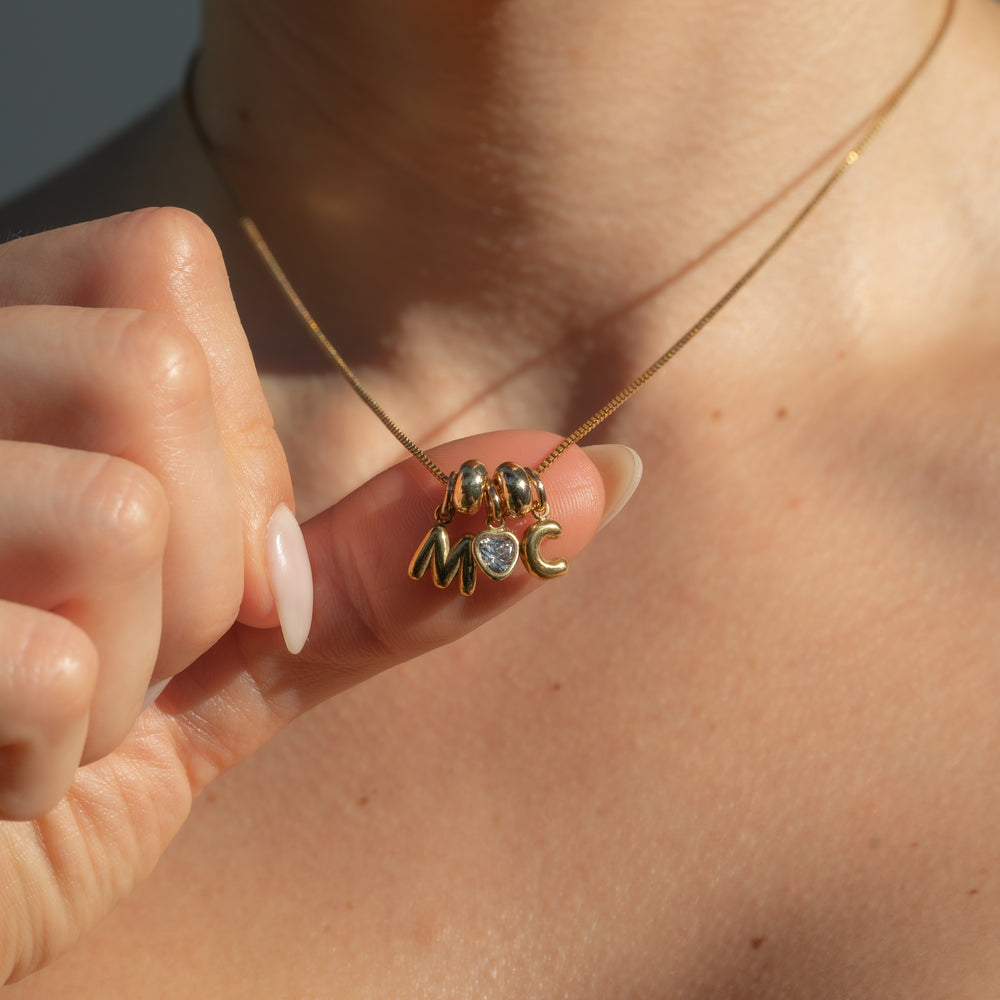 Gold necklace with charms held by a hand against a blurred background