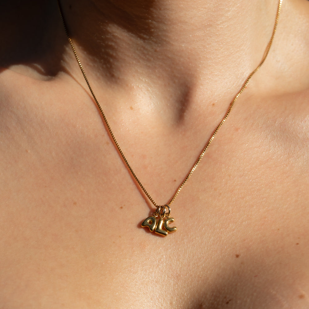 Gold venetian box chain necklace with a initial pendants on a person's neck