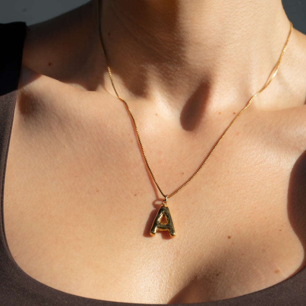 Gold-filled necklace with a letter 'A' pendant on a person's neck