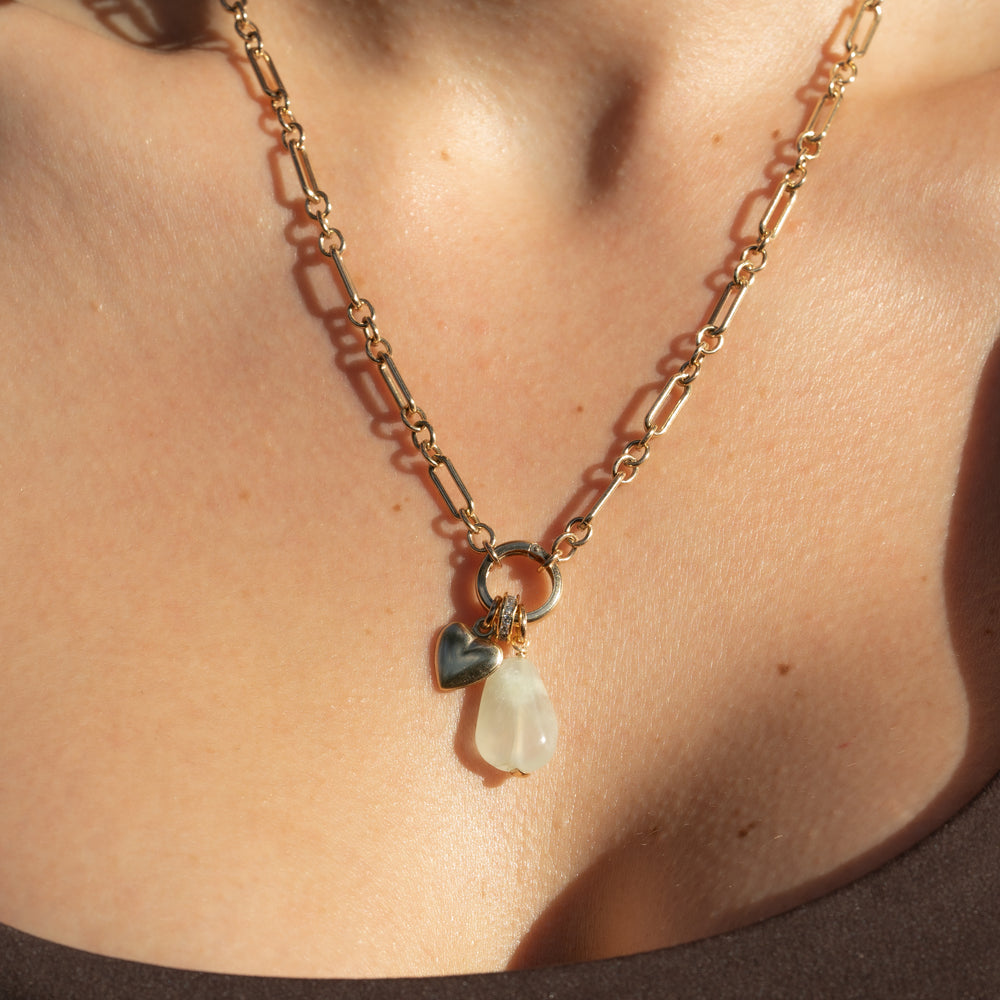 person wearing a long and short gold chain with a heart charm, a pave spacer and a gemstone. 