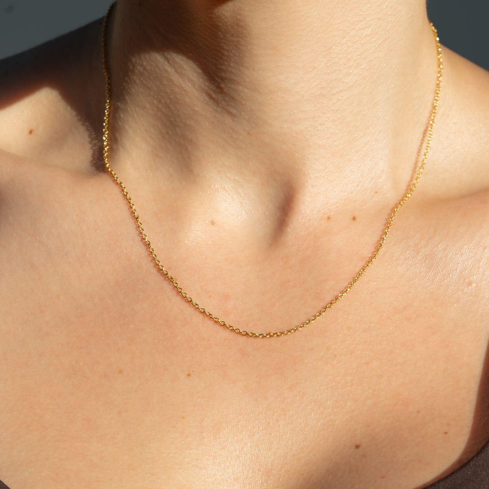 Gold dainty cable chain necklace on a person's neck with a neutral background