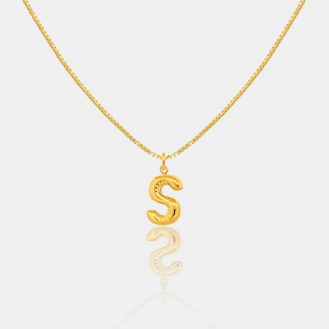 Gold necklace with a 'S' pendant on a light gray background