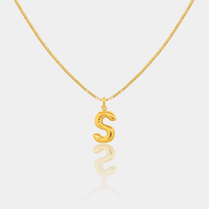 Gold necklace with a 'S' pendant on a light gray background