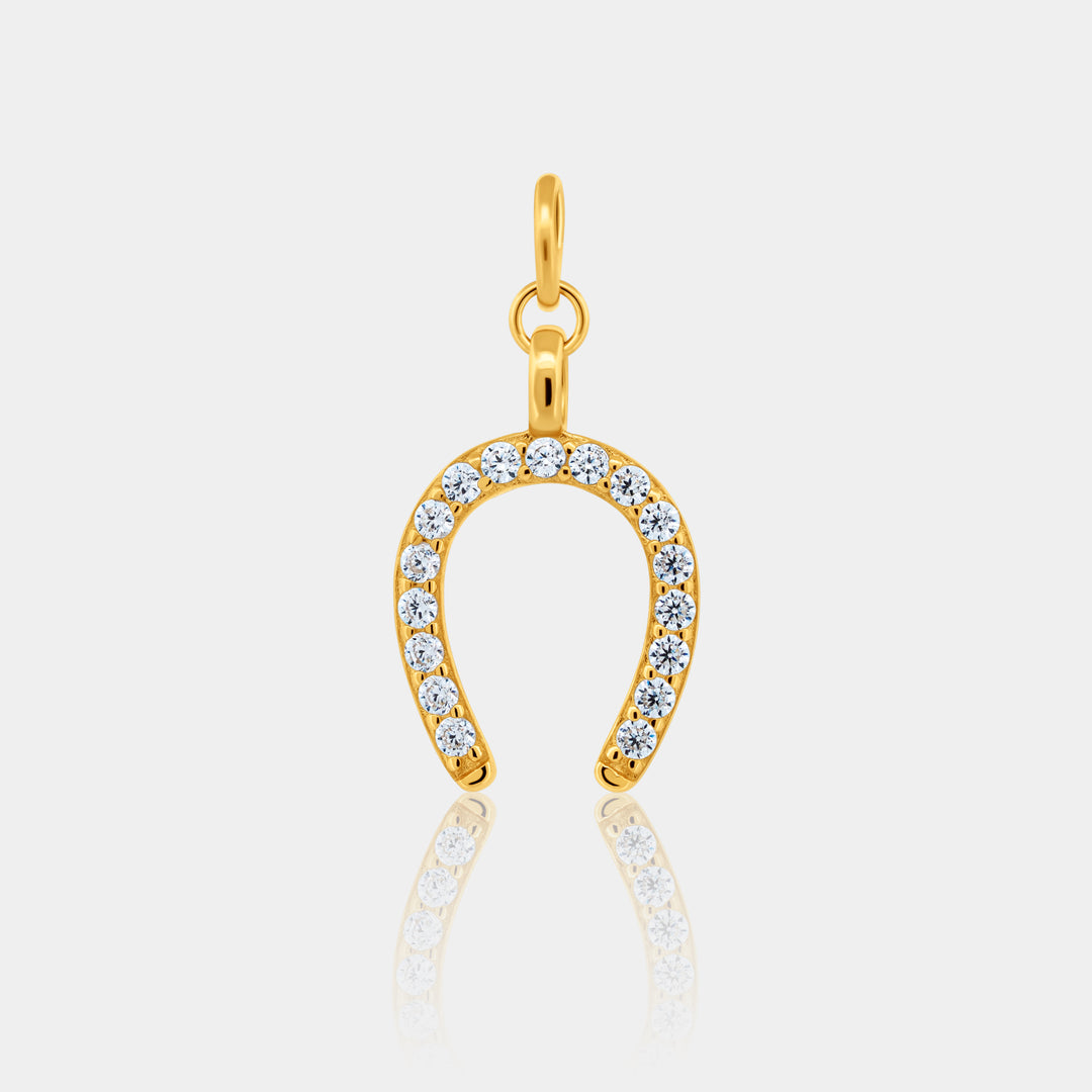 Gold horseshoe-shaped pendant with embedded stones on a light gray background