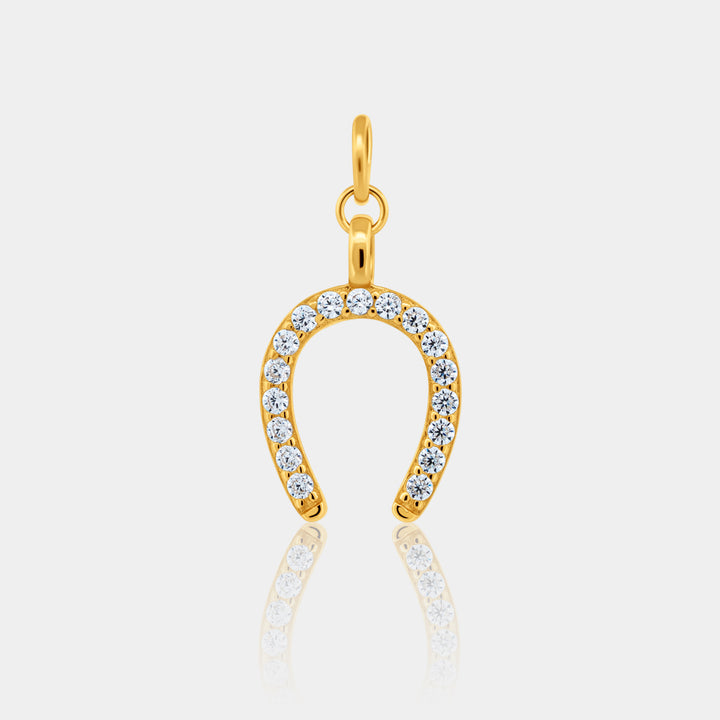 Gold horseshoe-shaped pendant with embedded stones on a light gray background