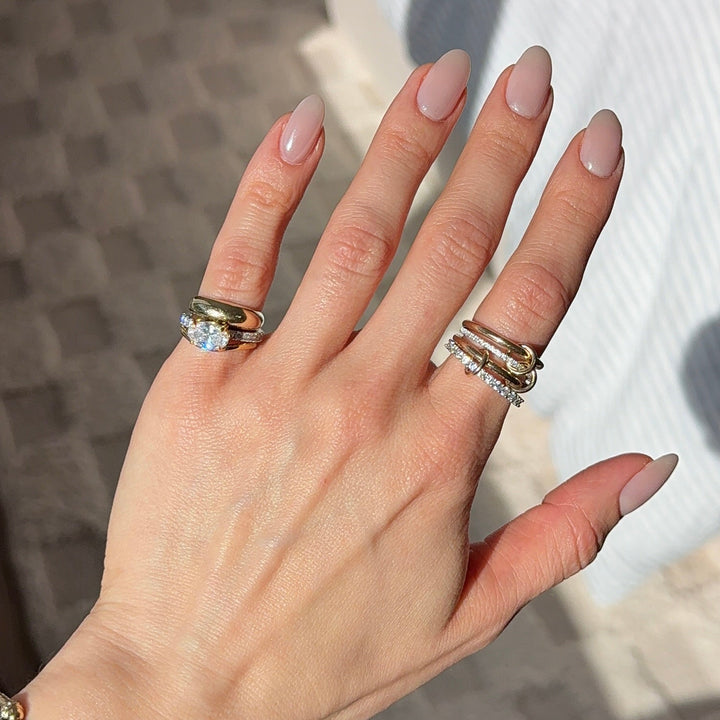 A hand showing a gold diamond solitaire pinky ring and other various ring designs