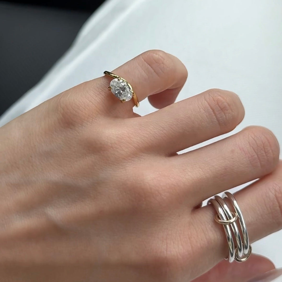 Hand wearing a gold ring with a diamond and a silver ring on a neutral background