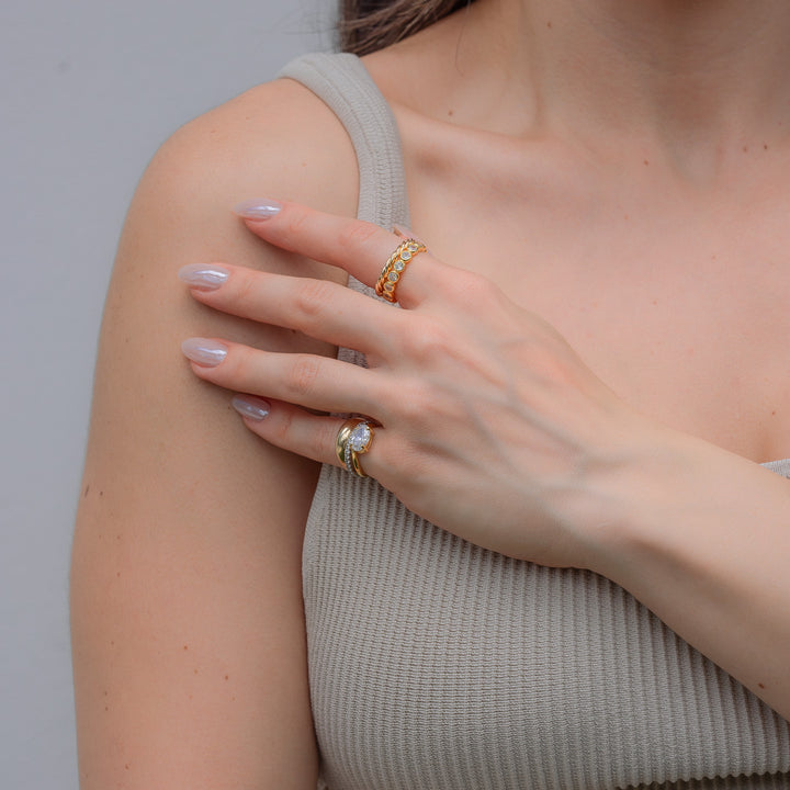 Close-up of a person wearing two gold rings on a neutral background