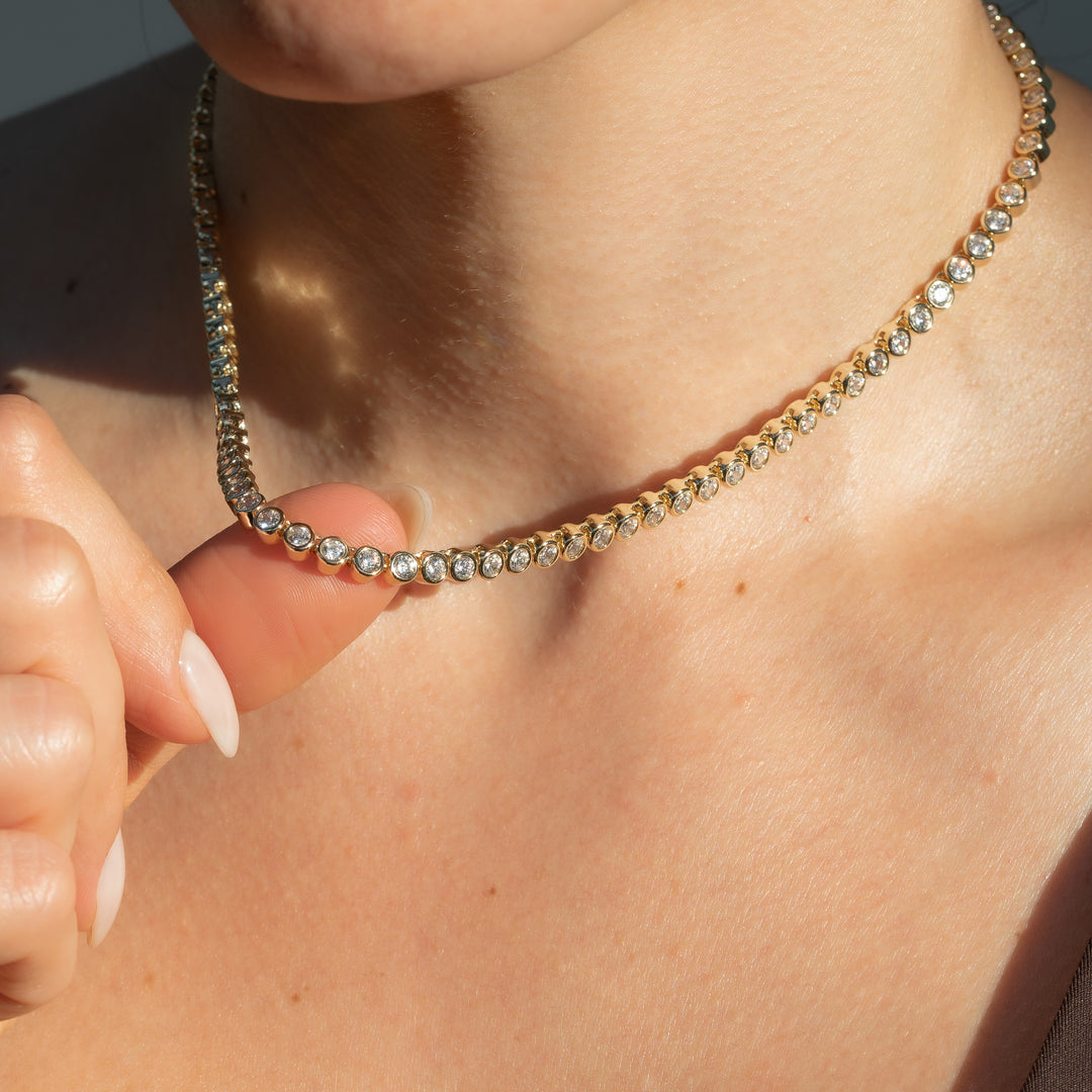Close-up of a person wearing a gold necklace with clear stones.