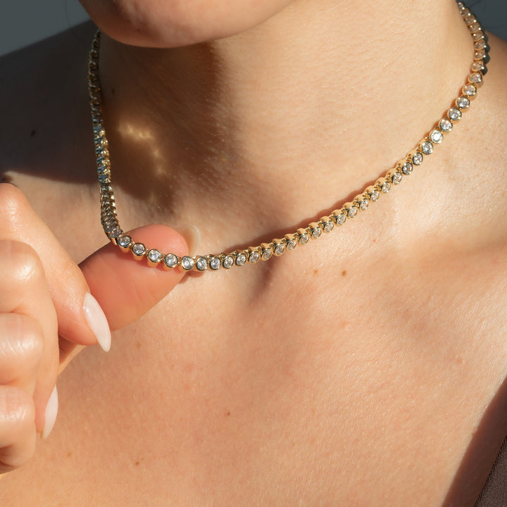 Close-up of a person wearing a gold necklace with clear stones.