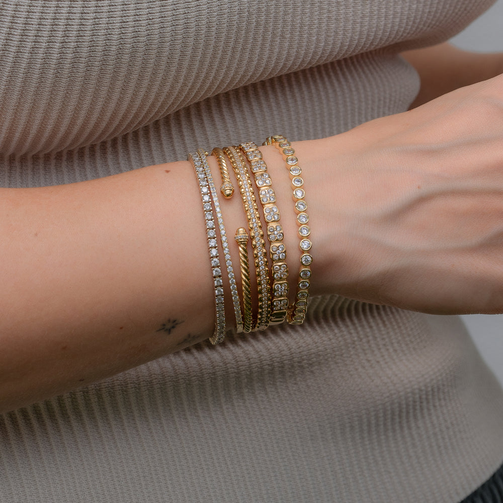 Stack of gold bracelets on a wrist against a neutral shirt