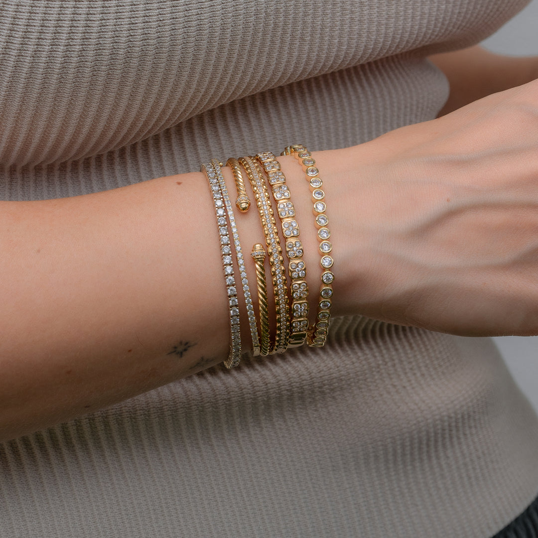 Stack of gold bracelets on a wrist against a neutral shirt