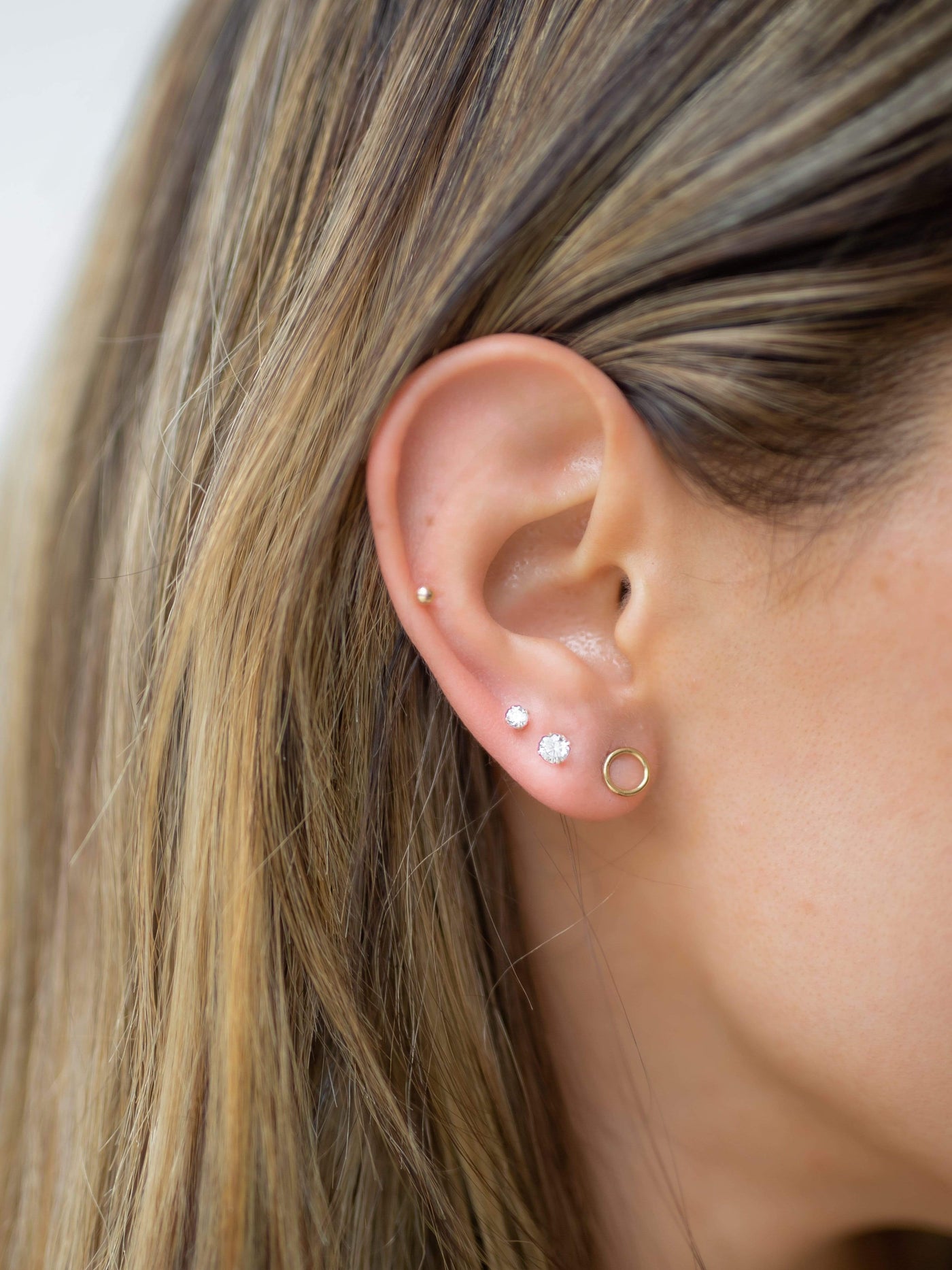 Ear showing different 14k gold fill earrings including a circle stud earring, 4mm cz stud earring and a 2mm ball earring