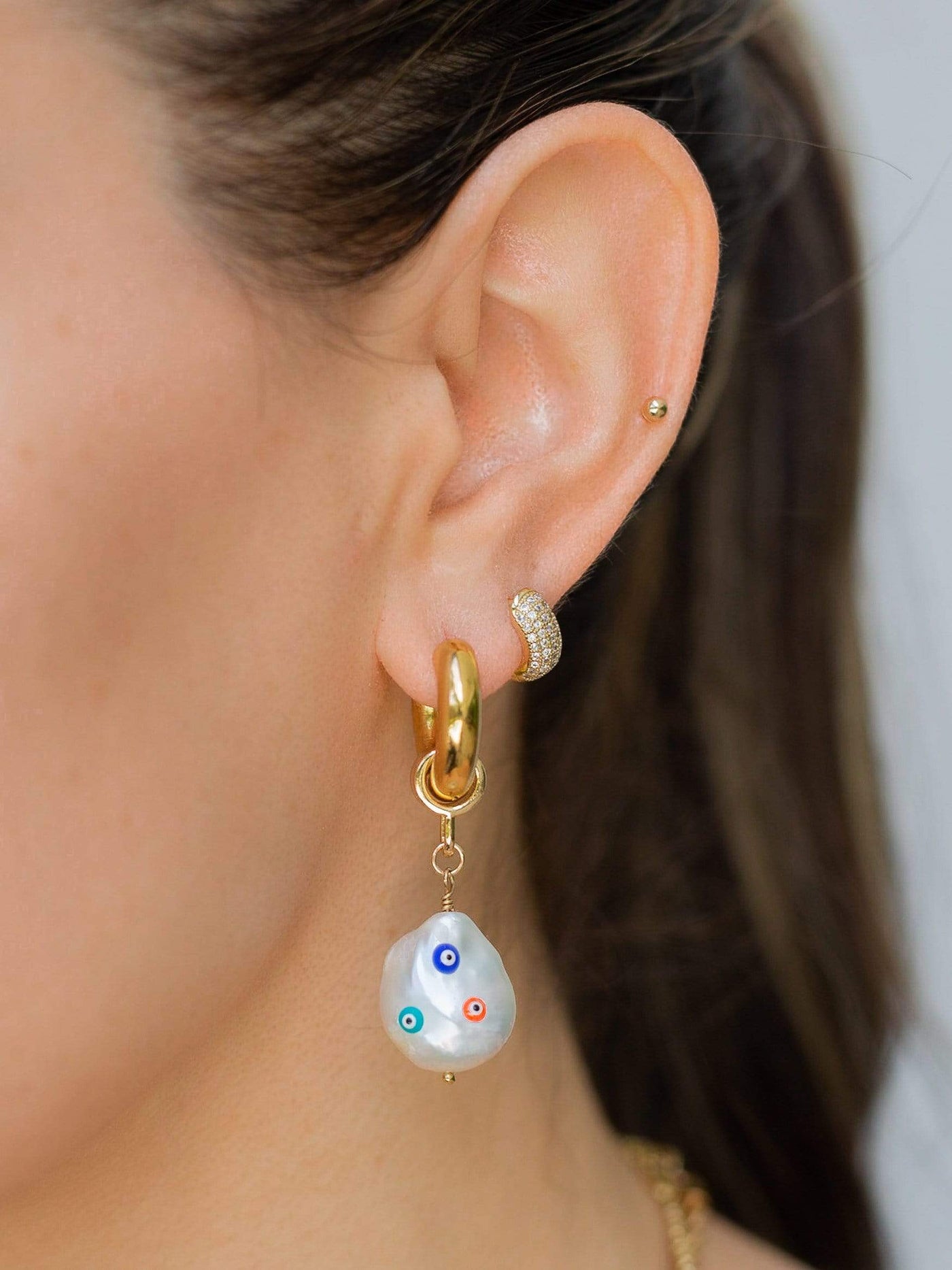 ear wearing a Gold Huggie Hoop with freshwater pearl drop evil eye charm