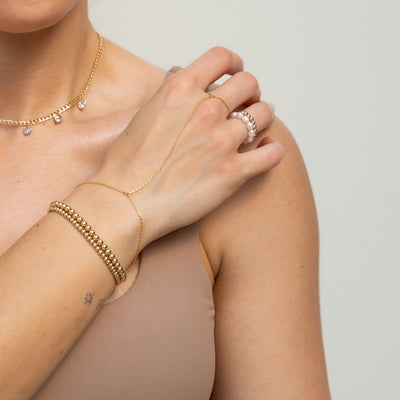 Model wearing Flat Box Rectangle Gold Hand Chain with Finger Loop along Pearl Ring and Gold Beaded Bracelets