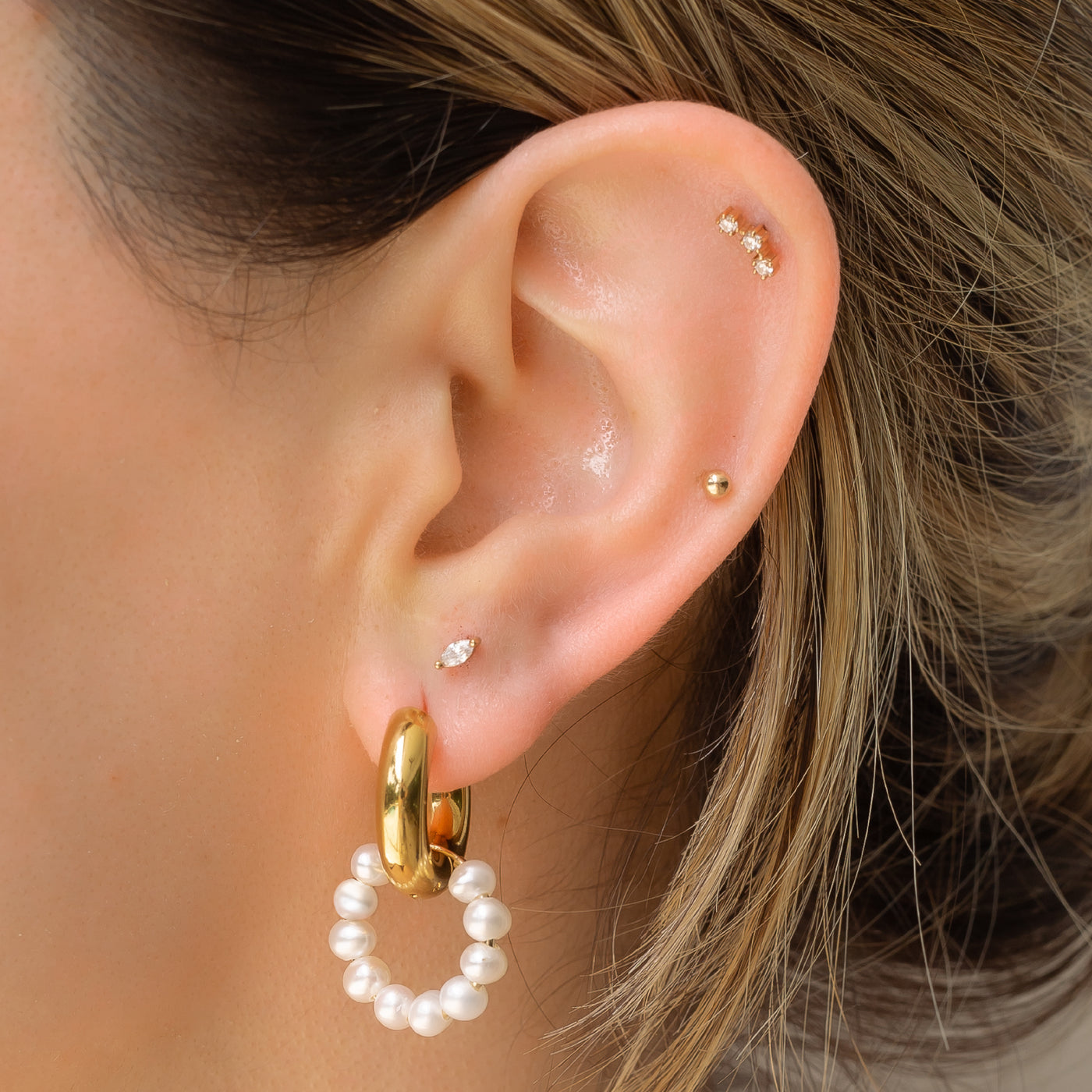 ear wearing gold huggie earrings and pearl hoops